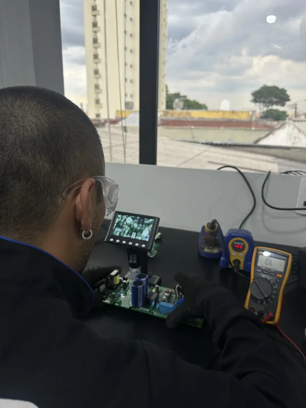 Técnico da WEB analisando uma placa de CLP com microscópio digital e multímetro