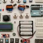 Componentes eletrônicos sobre a mesa: placa Arduino, sensores, display, servomotores e baterias
